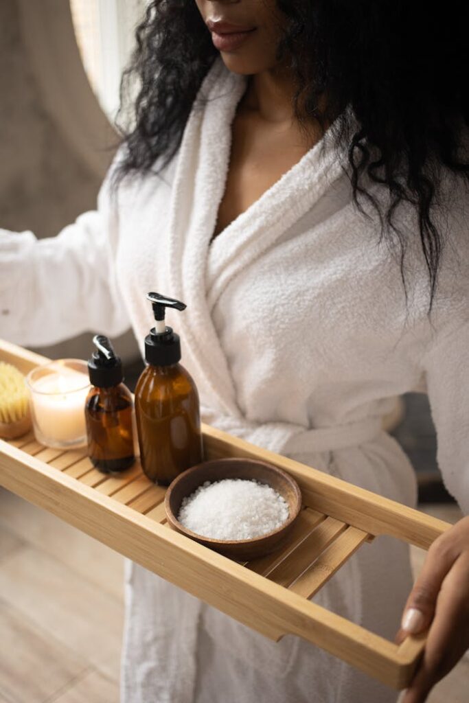 pexels-photo-6620839 A woman in a bathrobe holds a tray of natural spa products, focusing on self-care.